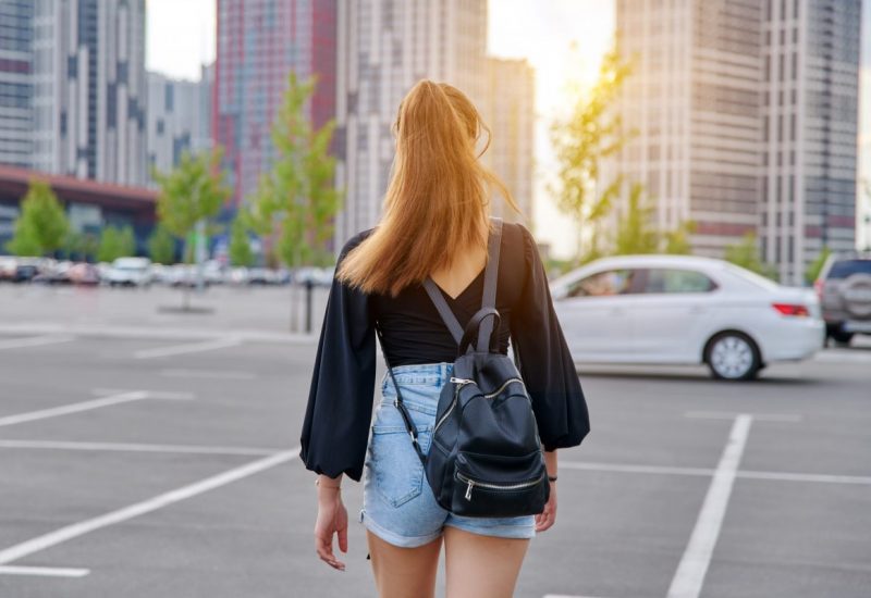 Back view of walking fashionable teenage girl with backpack, city, urban style background